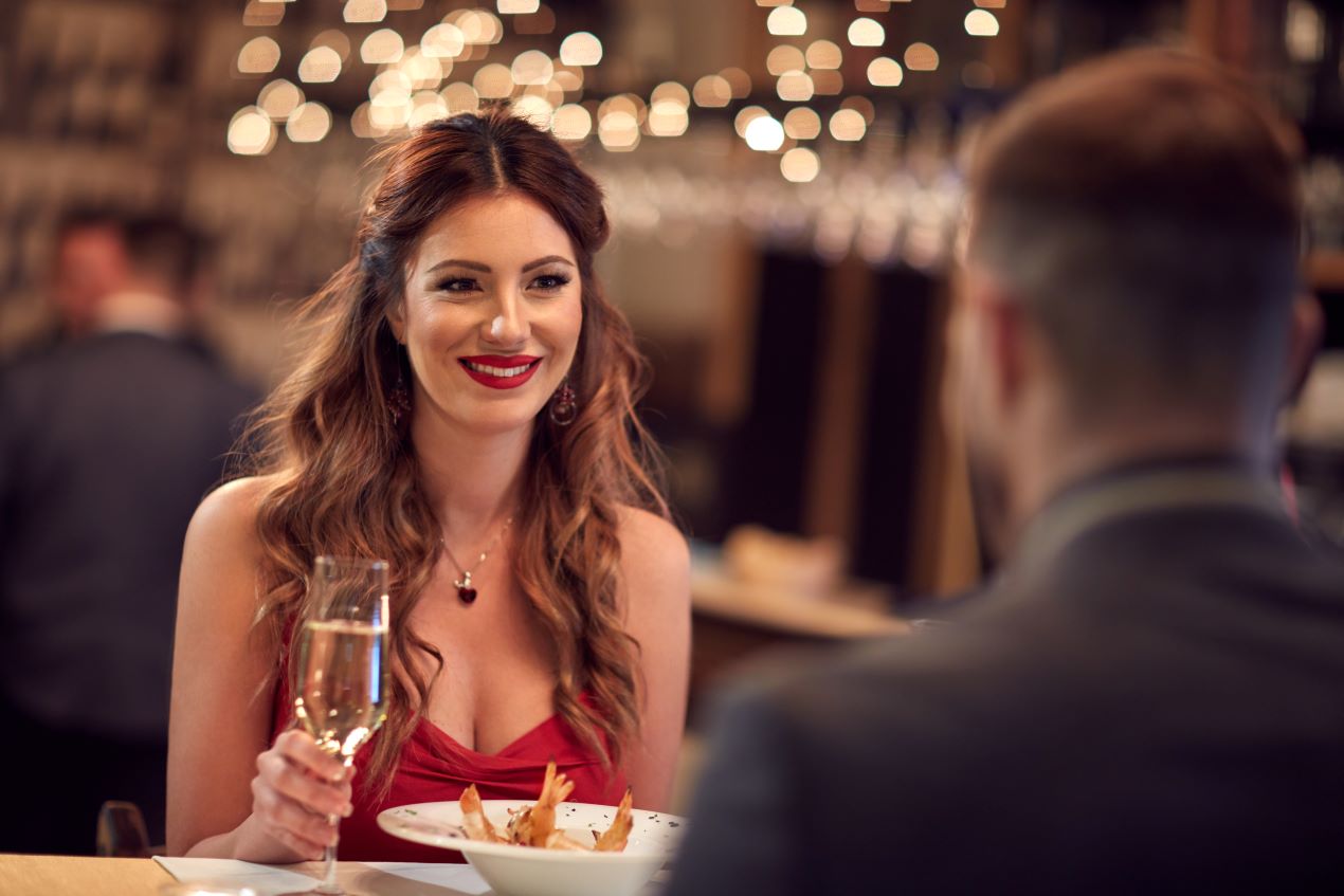 Eine elegante Frau in einem roten Abendkleid bei einem Candle-Light-Dinner – ideal für ein stilvolles Escort Frankfurt Erlebnis.